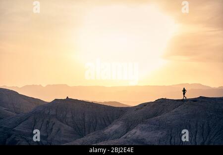 Athlète de coureur en silhouette qui couronne sur le sentier sauvage des montagnes dans le désert au coucher du soleil Banque D'Images