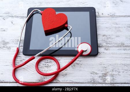 Stéthoscope en caoutchouc rouge avec tablette noire et coeur sur fond en bois Banque D'Images