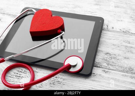 Stéthoscope en caoutchouc rouge avec tablette noire et coeur sur fond en bois Banque D'Images