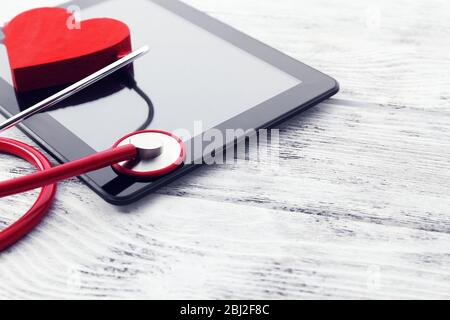 Stéthoscope en caoutchouc rouge avec tablette noire et coeur sur fond en bois Banque D'Images