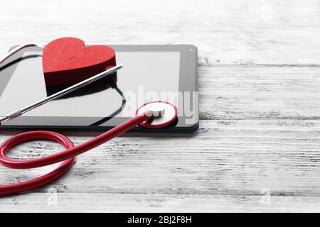 Stéthoscope en caoutchouc rouge avec tablette noire et coeur sur fond en bois Banque D'Images