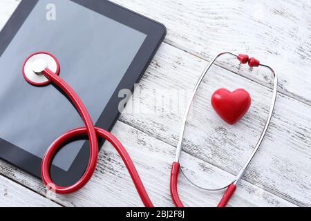 Stéthoscope en caoutchouc rouge avec tablette noire et coeur sur fond en bois Banque D'Images