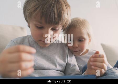 Deux enfants utilisant une tablette sur un canapé à la maison Banque D'Images