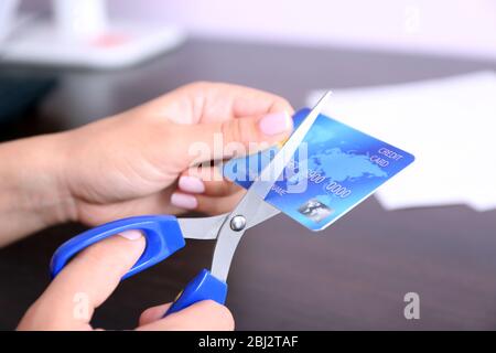 Les mains de la femme coupants la carte de banque avec des ciseaux sur fond de table en bois Banque D'Images