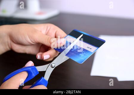 Les mains de la femme coupants la carte de banque avec des ciseaux sur fond de table en bois Banque D'Images