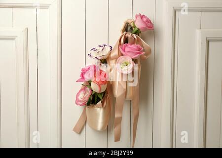 Chaussures de ballet décorées avec des roses dans elle accrochées sur un fond de mur en bois clair Banque D'Images