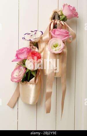 Chaussures de ballet décorées avec des roses dans elle accrochées sur un fond de mur en bois clair Banque D'Images