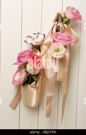 Chaussures de ballet décorées avec des roses dans elle accrochées sur un fond de mur en bois clair Banque D'Images