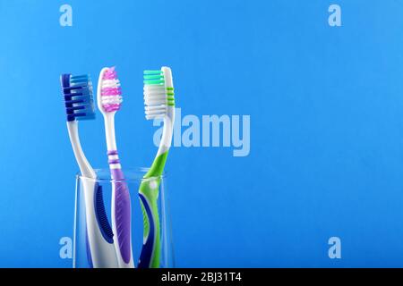 Trois brosses à dents dans une tasse en verre sur un fond bleu, placez pour votre texte Banque D'Images