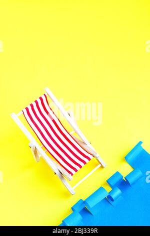 Chaise de terrasse rouge à rayures près de la mer. Fauteuil inclinable sur fond bleu et jaune. Concept repos d'été. Vacances. Banque D'Images