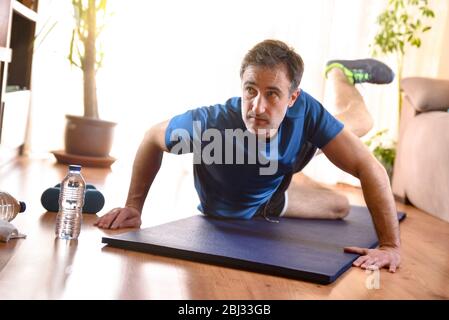 Homme faisant des exercices de jambes reposant sur un tapis dans son salon avec de l'eau et des haltères sur le sol Banque D'Images