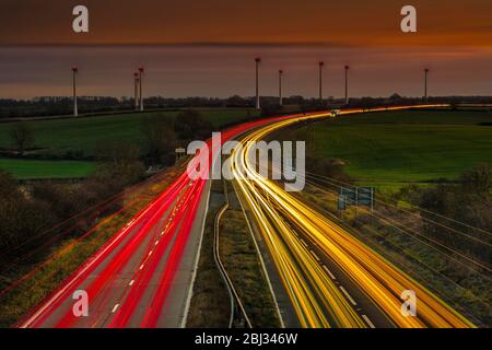 Light trails de véhicules sur une longue route à deux voies à la tombée de la nuit. Banque D'Images