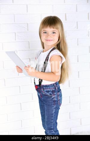 Petite fille avec tablette sur fond de mur de brique Banque D'Images