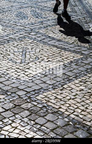 Walker avec des tuiles d'ombre et géométriques forme des formes et des motifs de lignes ondulées sur des pavés à Aveiro, Portugal Banque D'Images