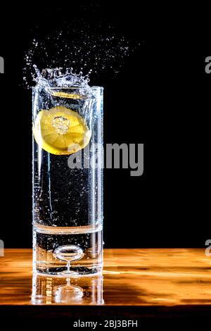 Une tranche de citron qui tombe dans un verre d'eau ou de liquide clair. Il y a une éclaboussure du citron qui frappe l'eau. Une simple actualisation de l'image Banque D'Images