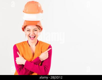 Concept publicitaire. Femme sur le visage souriant, architecte, ingénieur, fond blanc. La femme porte des tas de casques, espace de copie. Lady montre les points de geste avec le pouce vers le haut avec le doigt à l'espace vide. Banque D'Images