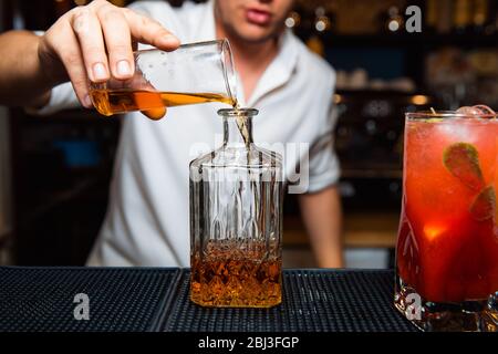 Le barman moure le whisky dans un décanteur transparent. Banque D'Images