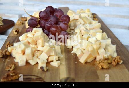 Un plateau rempli de délicieux plats faits pour une dégustation de fromage, contenant de petits morceaux de fromages durs, un raisin rouge et quelques noix de mur, naturel et biologique Banque D'Images