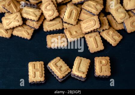 Le mot AIDE est écrit en majuscules. Beaucoup de cookies alphabet à proximité. Mise au point au premier plan. Espace de copie. Gros plan. Banque D'Images