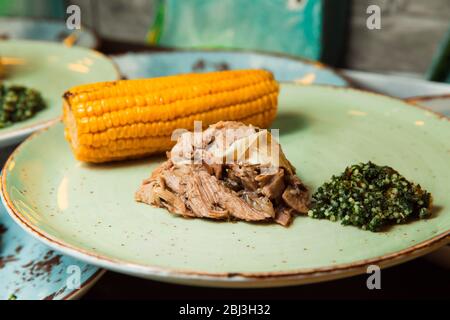 De la viande fraîche et juteuse est servie sur le rafle de maïs et de sauce verte. La nourriture se trouve sur une plaque ronde. Prêt à servir. Banque D'Images