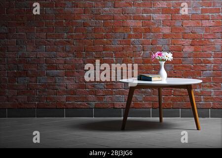 Table avec fleurs et livres sur fond de mur de brique Banque D'Images