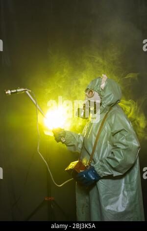 Concept de rayonnement, de pollution et de danger - l'homme dans des vêtements de protection et un masque à gaz sur fond sombre Banque D'Images