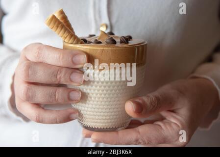 Les mains féminines tiennent le café de dalgon fait maison dans un verre avec du lait sur un support en bois. Café crémeux et tendance à la crème fouettée. Banque D'Images