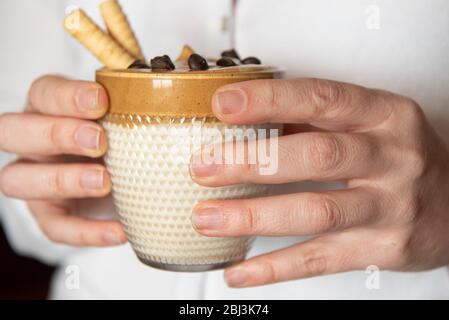 Les mains féminines tiennent le café de dalgon fait maison dans un verre avec du lait sur un support en bois. Café crémeux et tendance à la crème fouettée. Banque D'Images
