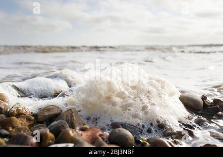 Gros plan sur une grande mousse de mer bouillonnante sur des galets avec des vagues qui s'écrasant en arrière-plan sur une plage britannique à Seasalter Kent, Angleterre Banque D'Images