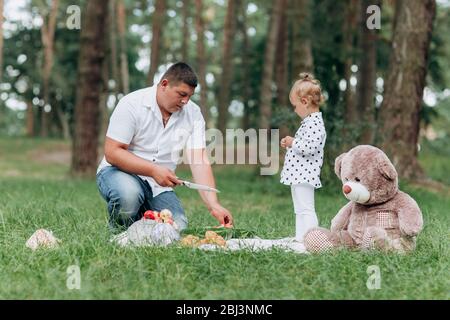 papa et petite fille pour pique-niquer dans le parc le jour de l'été. Le jeune père coupe le pastèque. Le père, le jour de bébé. Des vacances heureux Banque D'Images