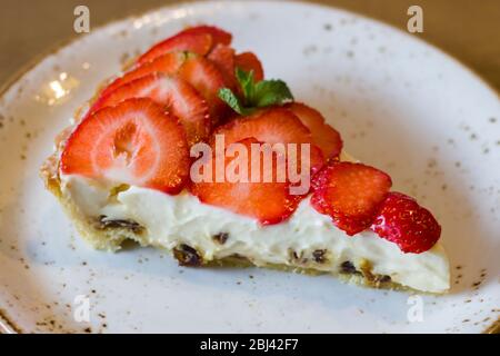 Un morceau de cheesecake avec fraises et feuilles de menthe sur une plaque Banque D'Images