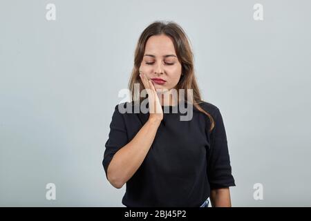 une fille fatiguée tient sa main sur sa joue de mal à la dent Banque D'Images