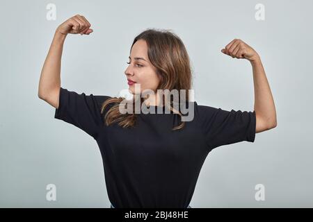 femme sur fond gris, forte fille montre des muscles, bras plié au coude Banque D'Images