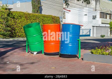 Trois poubelles à corps en métal vides pivotantes sur une base métallique sur un trottoir dans un jardin public urbain Banque D'Images