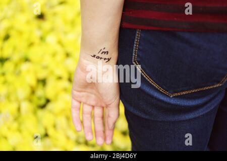 Main de la jeune femme avec une phrase tatouée sur elle, sur fond de fleurs jaunes, gros plan Banque D'Images
