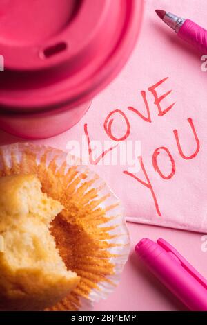 J'aime que vous avez écrit sur une serviette en papier près d'une tasse de café rose et d'un muffin mordu. Message romantique écrit sur une serviette rose Banque D'Images