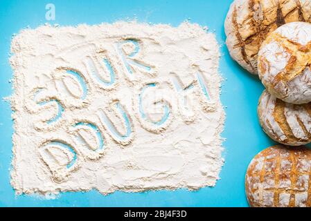 Pile de pain de levain maison cuit au four et le mot levain écrit dans la farine blanche. Vue sur le dessus avec pain fait maison sur un fond bleu Banque D'Images