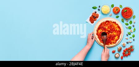 Femme non reconnaissable mettant la sauce tomate sur la pâte à pizza étirée à la main. Faire de la pizza classique chez soi avec des ingrédients frais. Banque D'Images