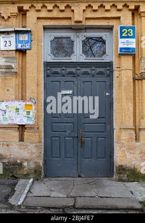 Porte en bois peinte en gris avec fenêtres ornées au-dessus et mur en briques jaunes anciennes. Détails architecturaux du bâtiment rétro dans la ville européenne Banque D'Images