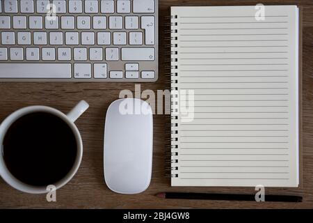 Vue panoramique sur un bureau à domicile avec clavier, café, souris et carnet en spirale avec espace de copie doublé pour les notes Banque D'Images