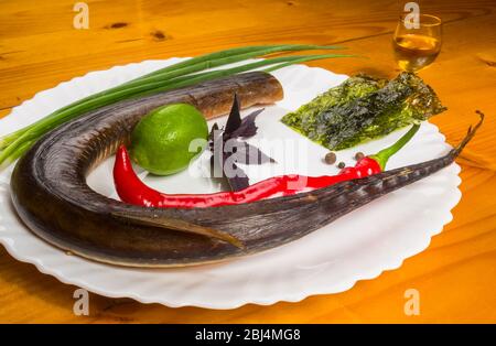 Still Life - orphie fumé avec de la chaux, le basilic, l'oignon vert, chili, nori chips, épices, huile d'olive dans un plat de céramique blanc, sur une table en bois Banque D'Images