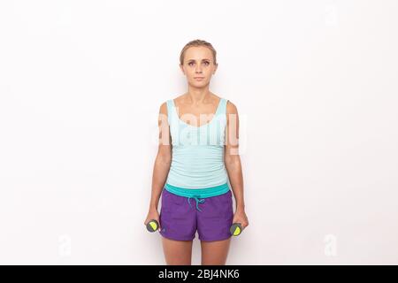 Une femme maigre dans un équipement sportif avec des haltères dans les mains sur fond blanc isolé. Banque D'Images