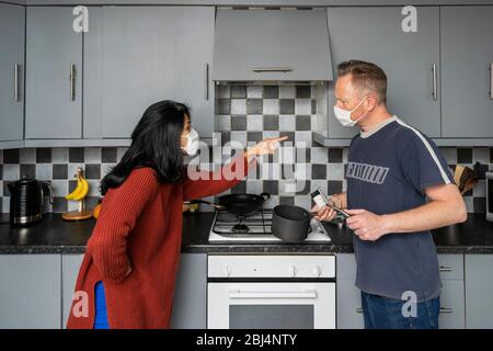 Couple en cuisine portant des masques de visage arguant pendant l'isolement de soi pendant le maintien, femme pointant sur l'homme Banque D'Images