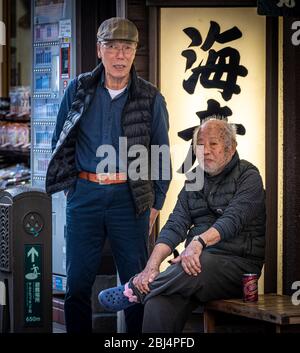 Deux hommes japonais âgés de la région qui regardent les gens qui passent et parlent. Enoshima, rue commerçante principale, île d'Enoshima, Japon Banque D'Images