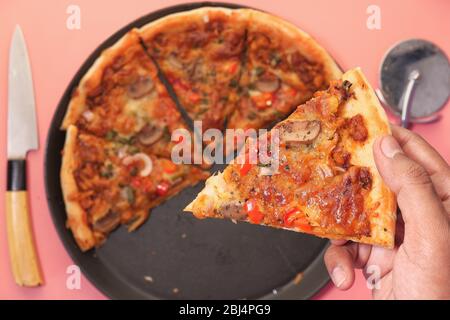 Femme prenant une tranche de délicieuse pizza sur fond rose Banque D'Images