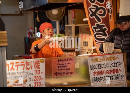 Un vendeur au marché alimentaire Nishiki à Kyoto Japon offrant des aliments à vendre. Banque D'Images