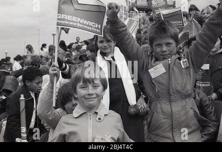 1984, 8 mai, des jeunes enthousiastes et historiques en dehors de fanions agitant en attendant l'apparition de sa Majesté la Reine de Greenwich pour l'ouverture officielle de la barrière de la Tamise, Charlton Riverside, Greenwich, Londres, Angleterre, Royaume-Uni. Banque D'Images