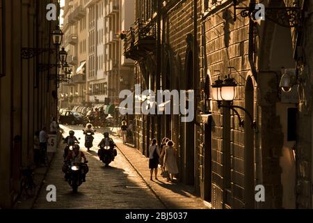 Des cyclomoteurs et des piétons dans une rue animée au coucher du soleil à Florence en Italie avec des bâtiments italiens classiques. Banque D'Images