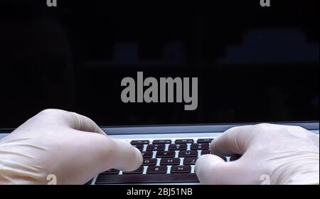 Regardez sur un médecin taper les mains sur un ordinateur portable tout en portant des gants médicaux contre des maladies comme la grippe ou le coronavirus. Banque D'Images