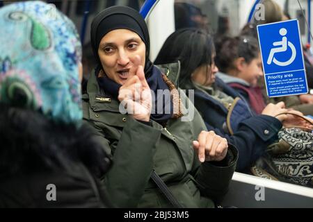 Une femme portant un foulard et faisant des gestes avec ses mains sur le métro de Londres, en Angleterre Banque D'Images